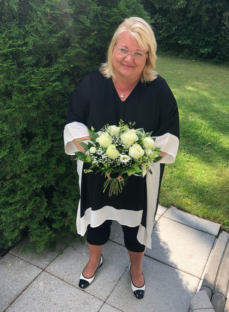 Sirpa Auervirta kuvattuna pihamaalla syntymäpäiväkukat kädessään.